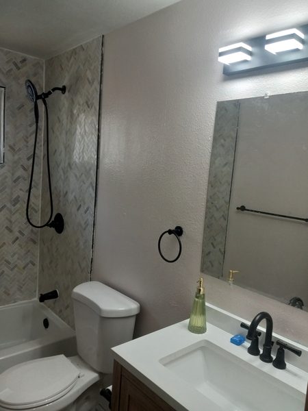 Completed bathroom with herringbone tile shower, black fixtures, and modern vanity