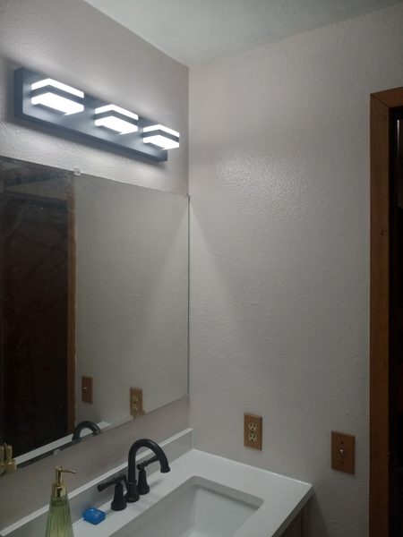 Modern LED vanity light fixture installed above bathroom mirror with black fixtures