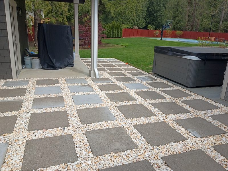 Beautiful paver patio with stone and gravel pattern, hot tub, and lush green backyard