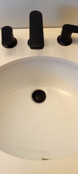 Close-up of matte black widespread faucet installed on white countertop